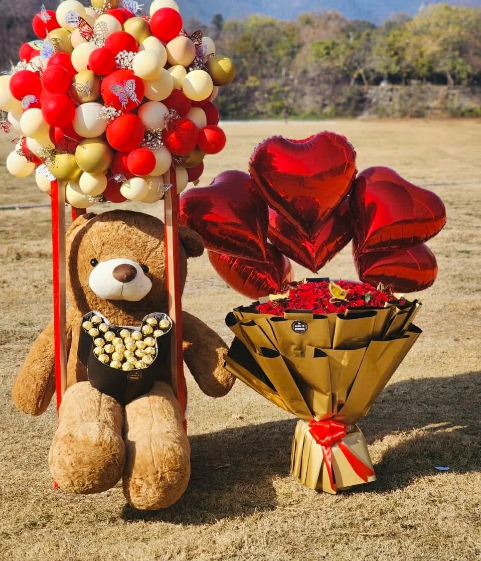 Luxury combo with 100 red roses and teddy bear inside balloon box in red and gold theme.
