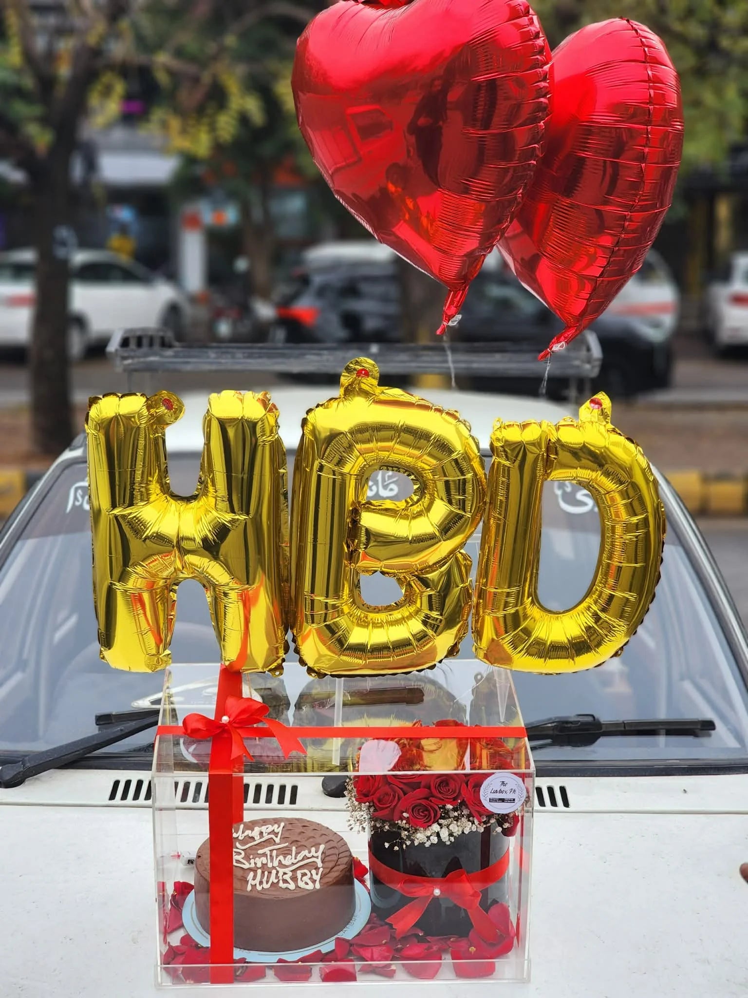 Luxury acrylic box with cake, flower arrangement and HBD balloons on top for birthday gifting.