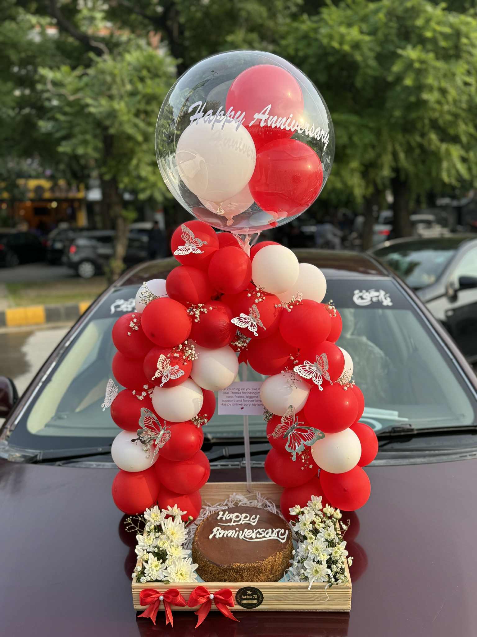 Luxury anniversary wooden tray with cake, red & white balloon arch, flowers, and custom message balloon – premium gift in Islamabad.