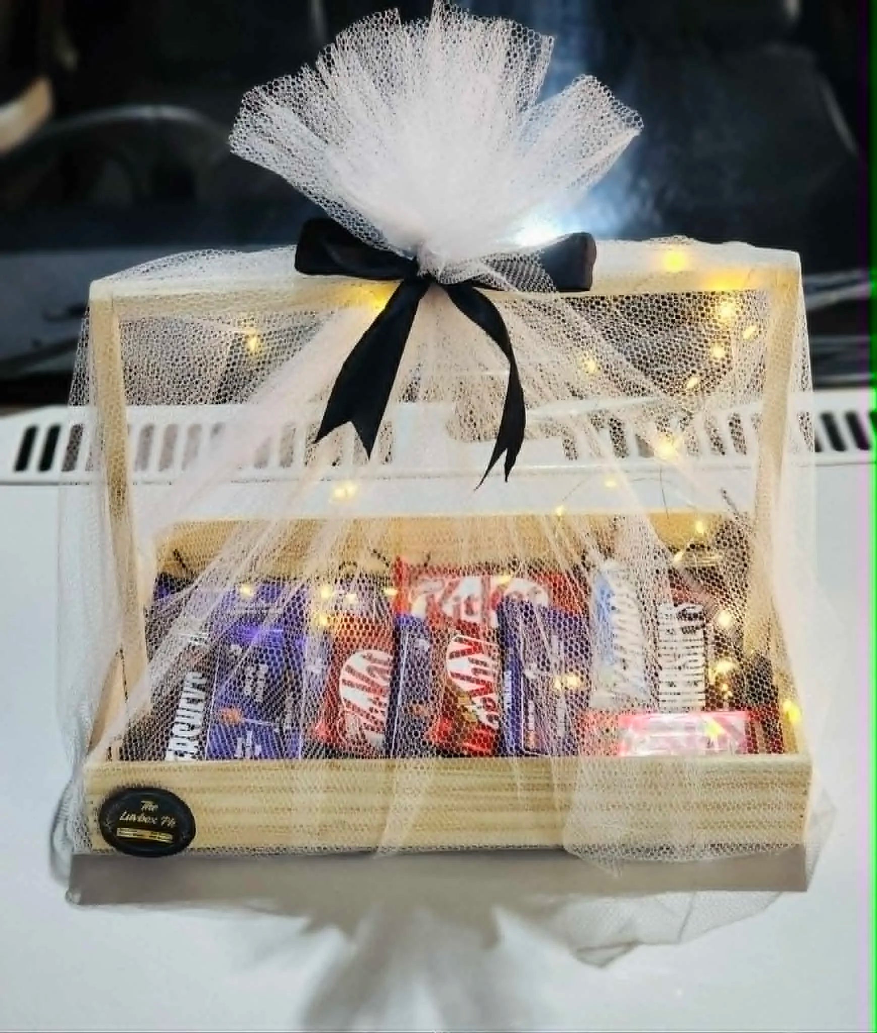 Medium wooden basket with chocolates covered in net and decorated with lights for gifting.