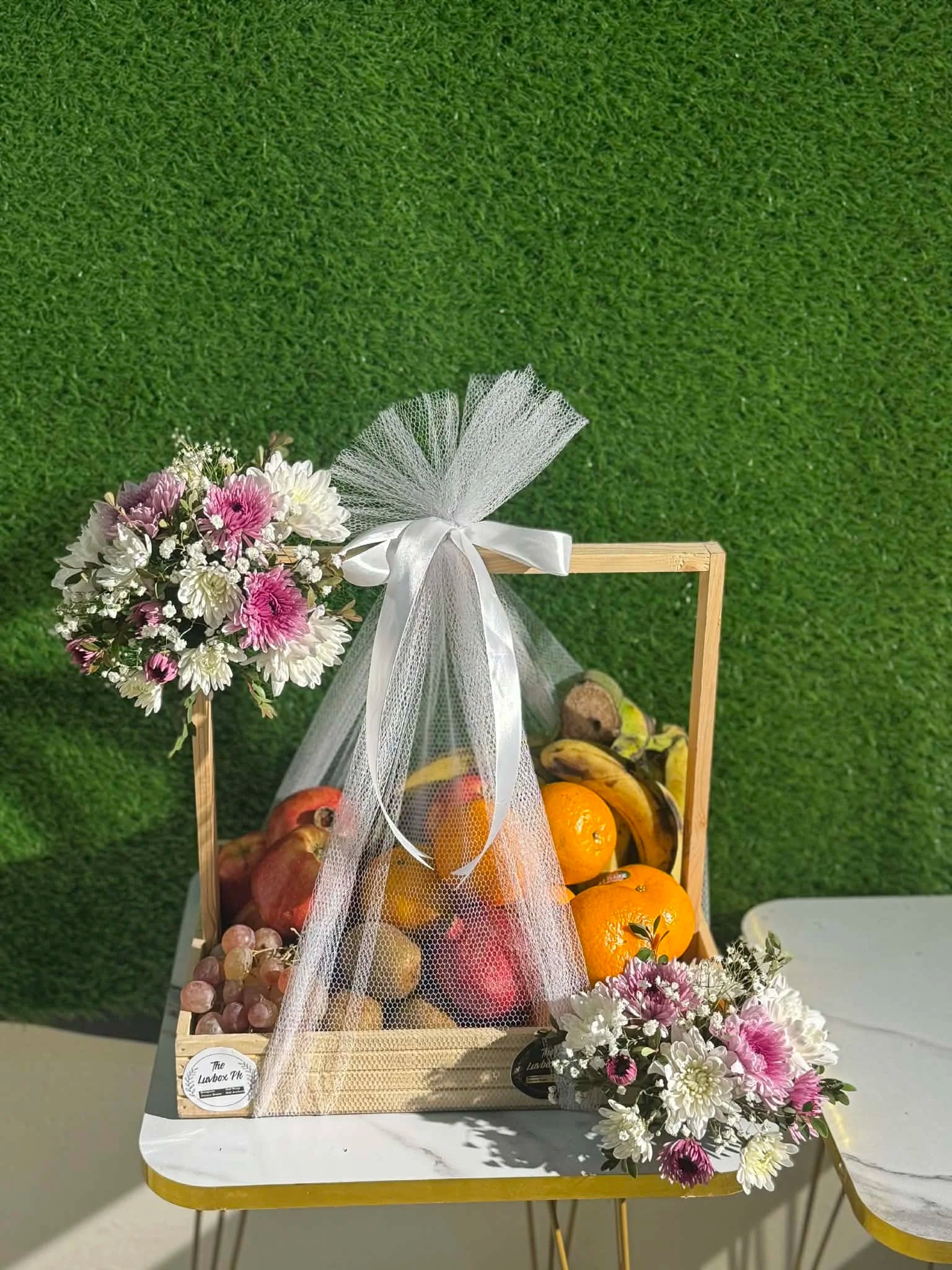 Luxury fruit basket with seasonal fruits in wooden tray with net and flowers Islamabad